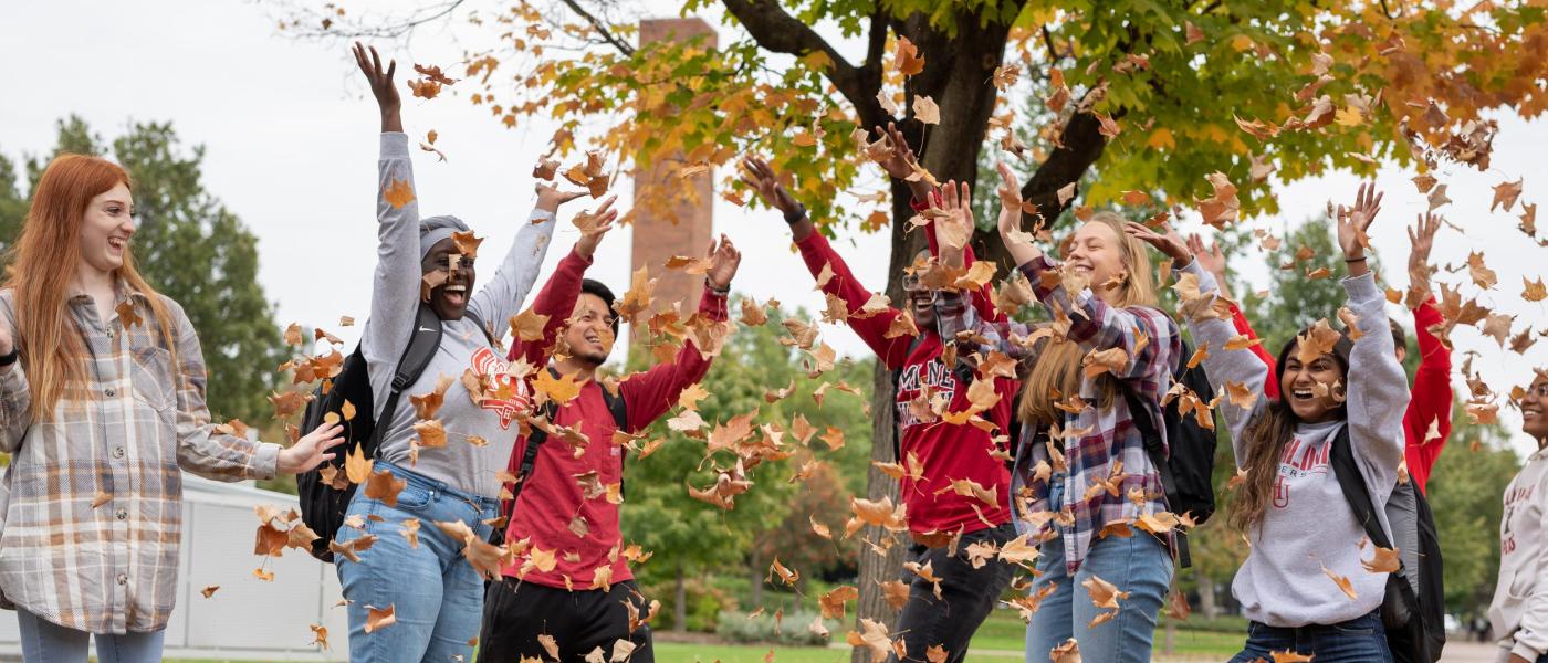 A group of students throwing fall leaves