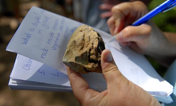 Hands holding rock and notebook in outdoor classroom